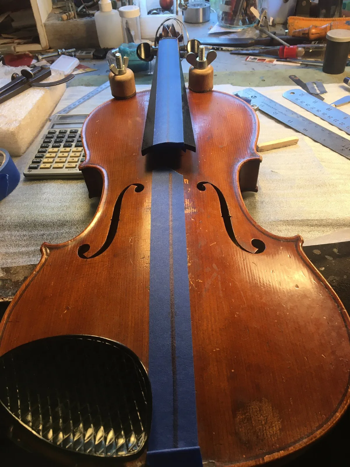 Unstrung violin with centre-line tape and clamps near the neck