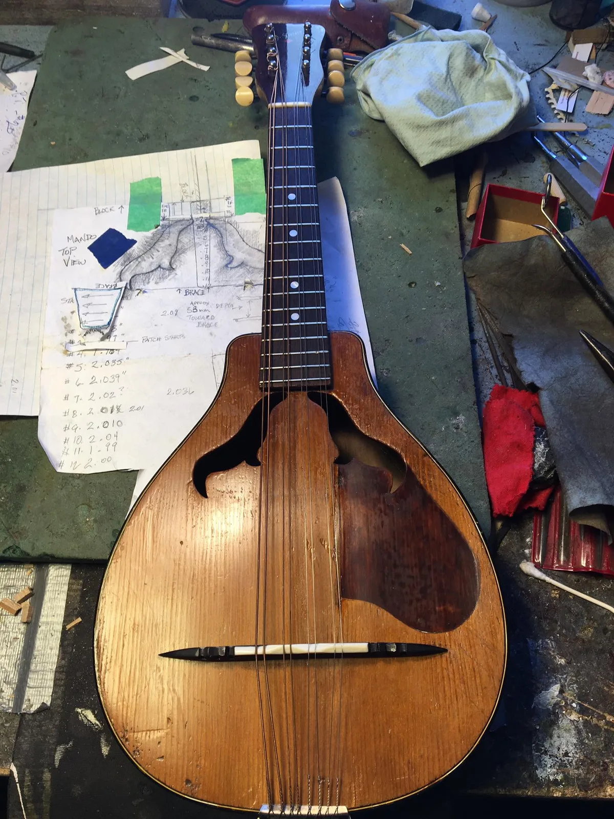 Mandolin on Peter’s repair bench beside hand-drawn repair notes and workshop tools
